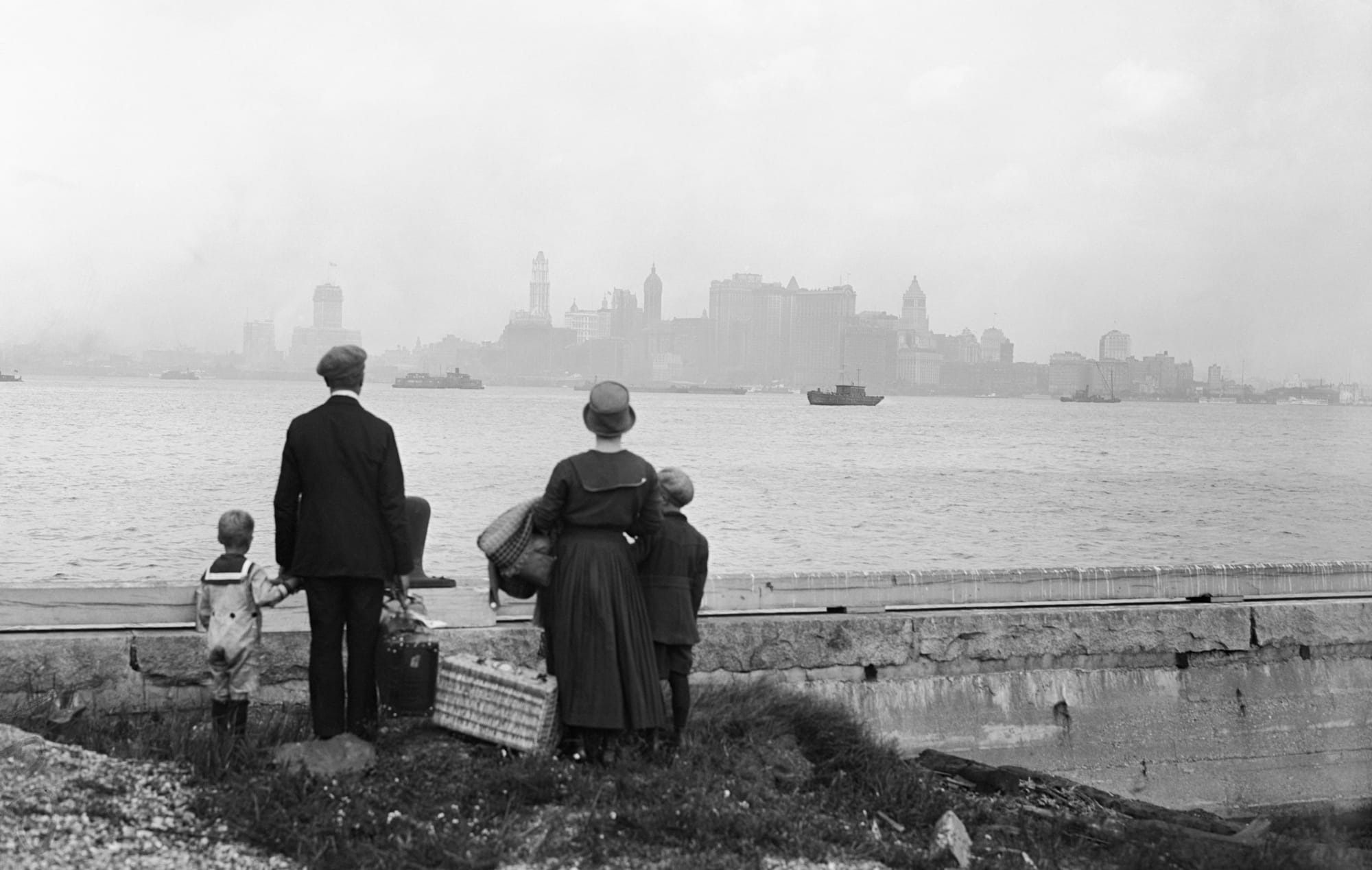 Une famille d'immigrants sur le quai d'Ellis Island après avoir juste passé l'examen rigide d'entrée dans le pays, regardant les toits de New York en attendant le ferry du gouvernement le 13 août 1925.